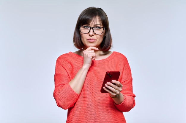 Foto mujer de mediana edad con teléfono inteligente en manos con expresión facial de pensamiento pensativo