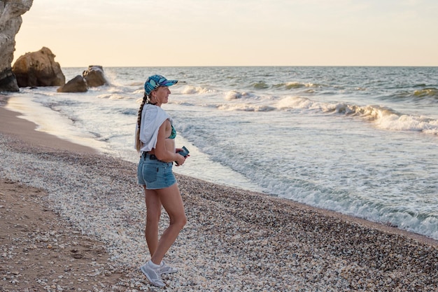 Una mujer de mediana edad con una trenza en una gorra y pantalones cortos en la costa de viajes y turismo