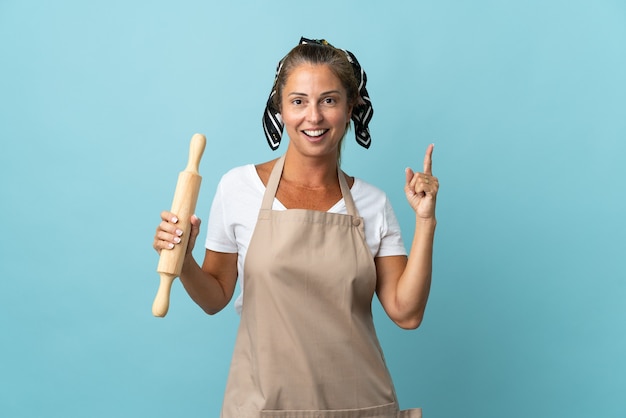 Mujer de mediana edad en uniforme de chef pensando en una idea apuntando con el dedo hacia arriba