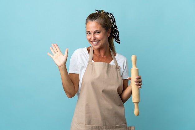 Mujer de mediana edad en uniforme de chef saludando con la mano con expresión feliz