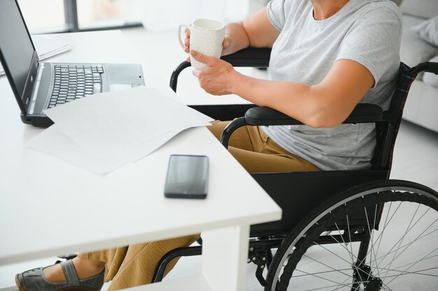 Mujer de mediana edad usando laptop sentada en silla de ruedas en casa