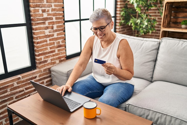 Mujer de mediana edad usando laptop y tarjeta de crédito en casa