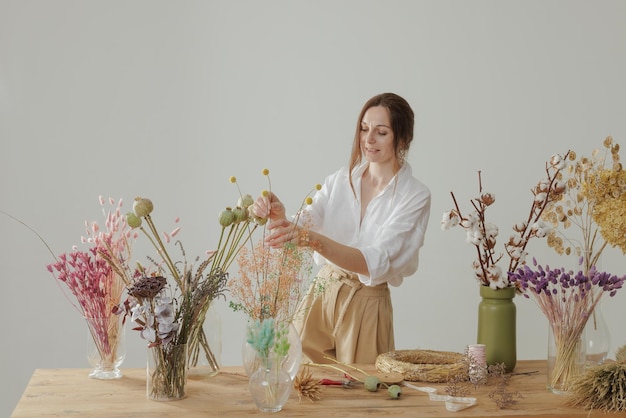 Mujer de mediana estatura que trabaja con flores secas ensambla la decoración de composición y el concepto de floristería