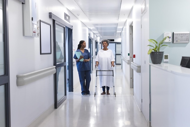 Una mujer médica afroamericana caminando con una anciana paciente con muletas en el pasillo del hospital