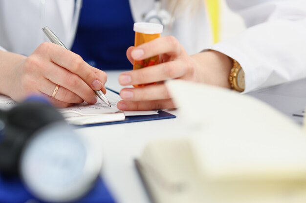 Mujer medicina doctor mano sostenga el tarro de píldoras y escriba la receta al paciente en la mesa de trabajo. Panacea y salvavidas, tratamiento de prescripción, concepto de farmacia legal. Formulario vacío listo para ser usado