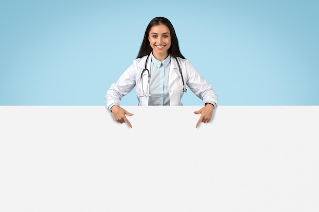 Mujer médico apuntando a una pancarta vacía comportamiento feliz