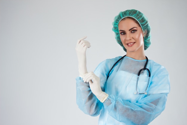 Mujer médico Cirujano en matorrales con sombrero médico poniendo guantes quirúrgicos.