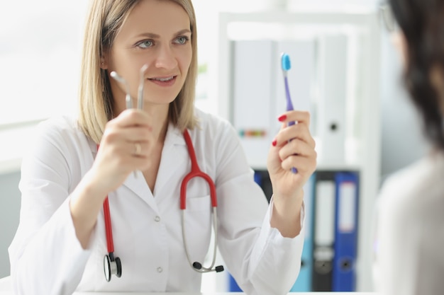 La mujer médico dentista muestra el cepillo de dientes del paciente y el instrumento dental higiene oral y odontología