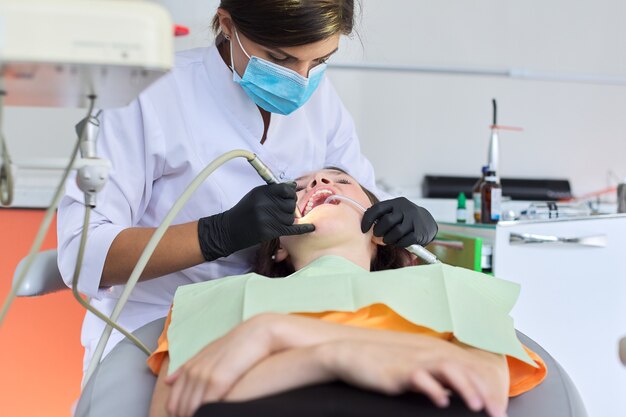 Mujer médico dentista tratar dientes a paciente niña en consultorio dental