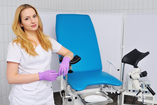 Mujer médico ginecólogo apoyado en una silla ginecológica azul