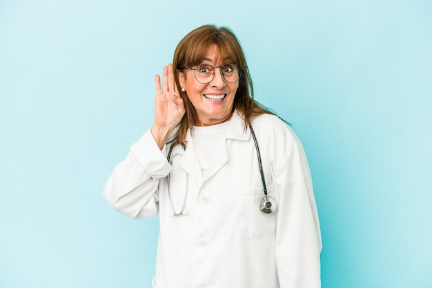 Mujer médico de mediana edad aislada sobre fondo rosa tratando de escuchar un chisme.