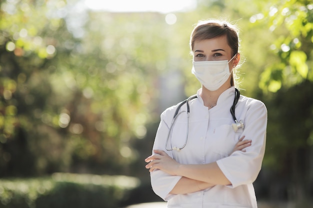 Mujer médico o enfermera con una máscara protectora en el parque entre los árboles.