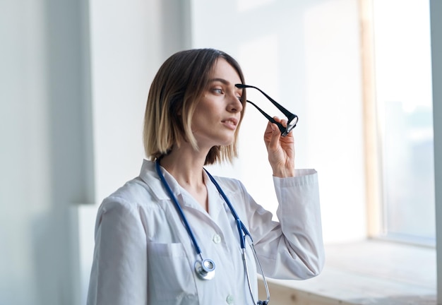 Mujer médico profesional con gafas en la mano y un estetoscopio alrededor de su cuello