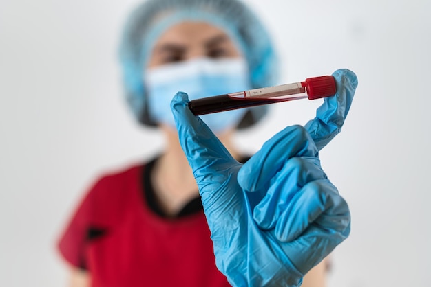 mujer médico usar uniforme rojo protección de máscara y guantes sostener tubo de ensayo con muestra de sangre