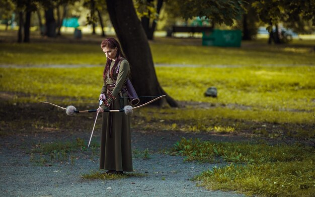 Mujer medieval guerrera con arco de caza en bosque verde