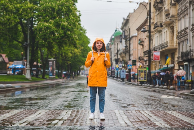 Mujer en medio de la calle cruzando la calle con impermeable amarillo