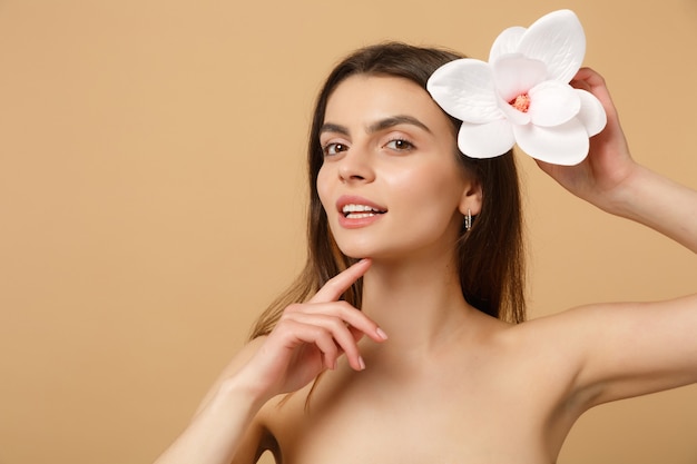 Mujer medio desnuda morena de cerca con una piel perfecta, maquillaje desnudo aislado en la pared de color beige pastel