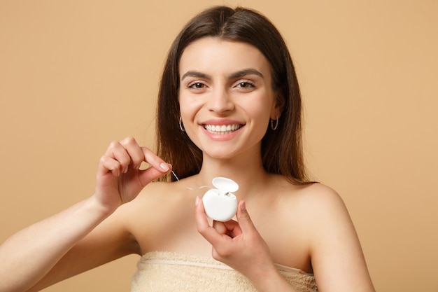 Mujer medio desnuda morena de cerca con una piel perfecta, maquillaje desnudo con hilo dental aislado en la pared de color beige pastel