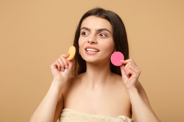 Mujer medio desnuda morena de cerca con una piel perfecta, quitando el maquillaje desnudo aislado en la pared beige pastel