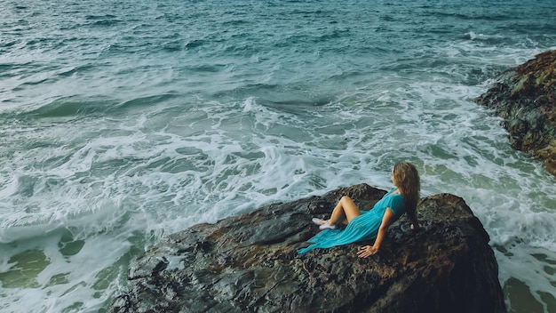 La mujer medita se relaja en una colina de arrecife de roca en la mañana tormentosa lluvia mar nublado Concepto femenino relajarse salud sexual Vista de silueta dramática oscura