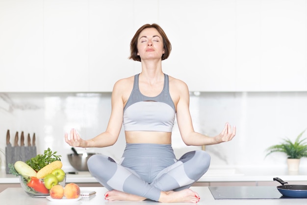 Mujer meditando en la cocina rodeada de comida saludable