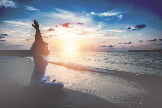 Foto mujer meditando mientras está sentada en la playa durante la puesta de sol