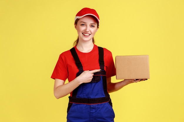 Mujer mensajera sonriente de pie y señalando el pedido en línea del paquete de cartón para el cliente