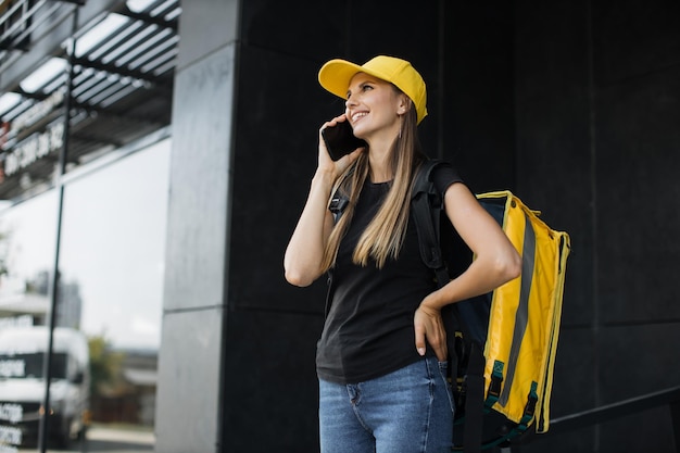 Mujer mensajera con teléfono móvil buscando dirección de entrega de comida de un restaurante