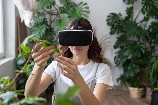 Mujer del metaverso de jardinería doméstica usando gafas vr en invernadero tocando la realidad aumentada de la planta