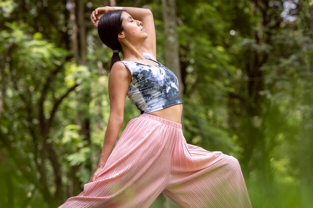 Mujer mexicana haciendo yoga con diferentes posturas en el parque al aire libre con césped y árboles