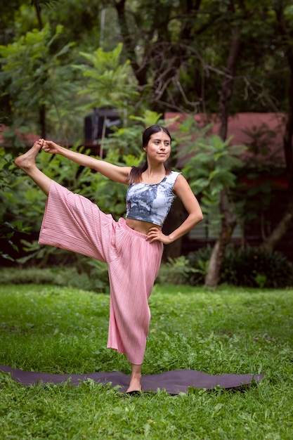 Mujer mexicana haciendo yoga con diferentes posturas en el parque al aire libre con césped y árboles