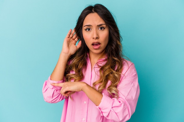 Mujer mexicana joven aislada en azul tratando de escuchar un chisme.