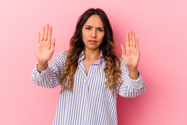 Mujer mexicana joven aislada en la pared rosada que se coloca con la mano extendida que muestra la señal de stop, impidiéndole.