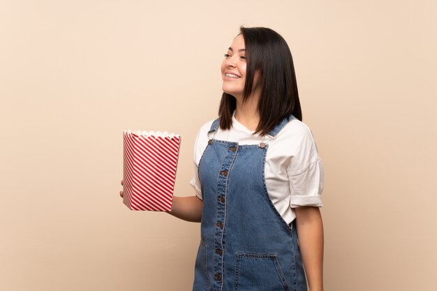 Mujer mexicana joven sobre el fondo aislado que sostiene un cuenco de palomitas