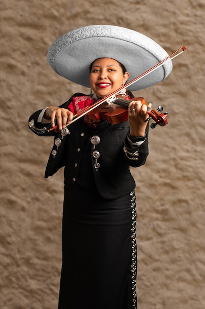 Foto mujer mexicana mariachi mujer sonriente tocando violín mariachi traje de niña sobre un fondo de pared de arcilla