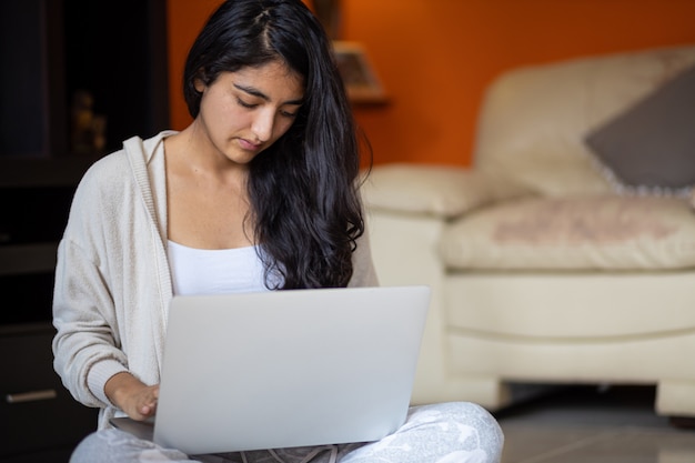 Mujer mexicana sentada en la sala de estar con laptop