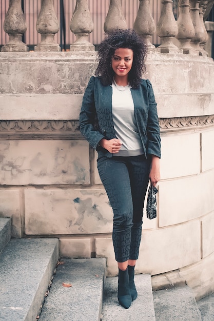 Mujer mezclada joven con el peinado afro que sonríe en fondo urbano. Chica negra con ropa casual.