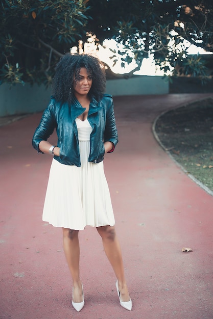 Mujer mezclada joven con el peinado afro que sonríe en fondo urbano. Chica negra con ropa casual.