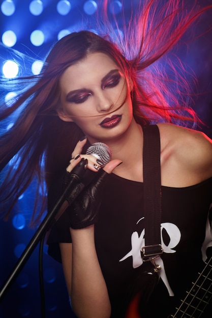 Mujer con un micrófono y una guitarra en la mano en el escenario cantando una canción en estilo rock