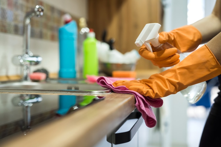 Foto mujer mientras limpia la superficie de un escritorio de cocina con una esponja en sus guantes de goma. tareas del hogar