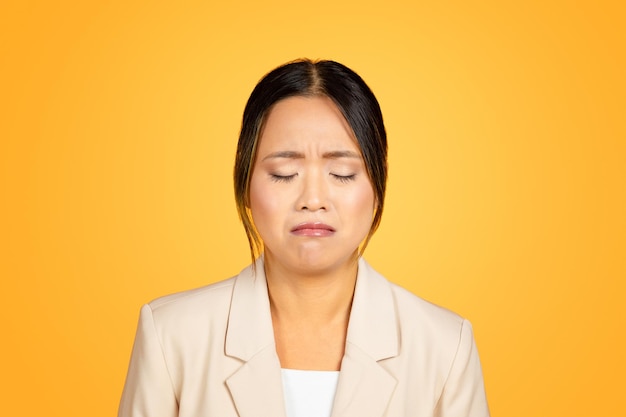Mujer milenaria asiática llorando emocionalmente en marcado contraste con un telón de fondo de estudio naranja brillante