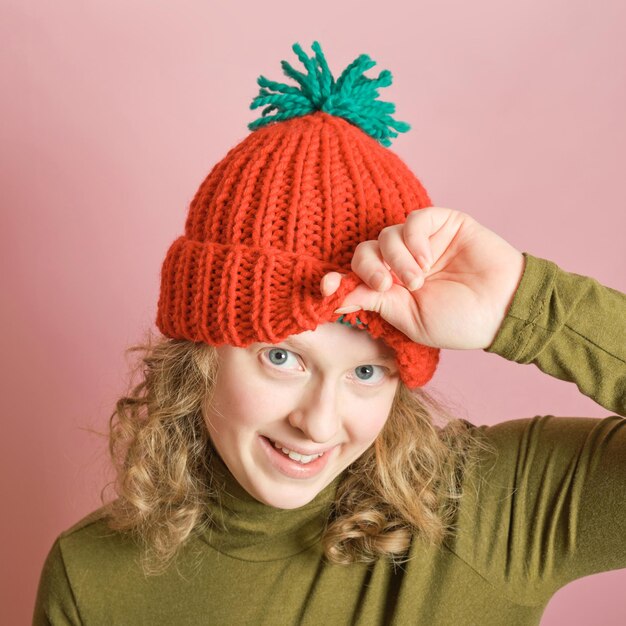 Foto mujer milenaria juguetona se divierte usando gorro de punto rojo de invierno sobre fondo rosa concepto de moda de invierno