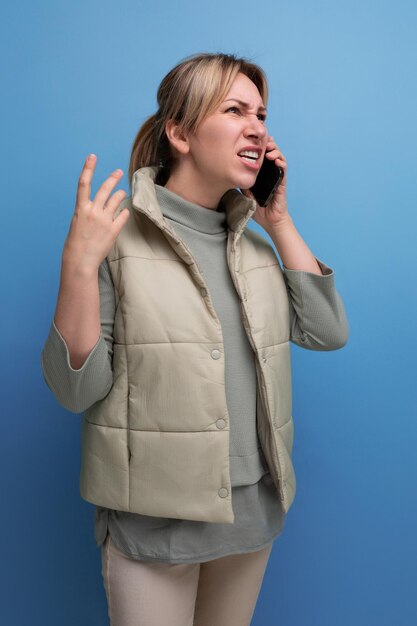 Mujer milenaria rubia hablando por teléfono con un fondo azul aislado