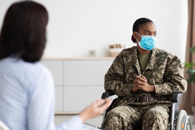 Mujer militar negra deprimida en silla de ruedas con sesión de terapia con psicólogo