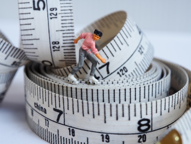 Mujer miniatura que patina en la cinta de medición, pensando en la pérdida de peso y el cuerpo delgado.