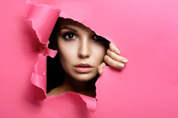 La mujer mira en el agujero de papel de color rosa, maquillaje y cosméticos de belleza de moda, salón de belleza