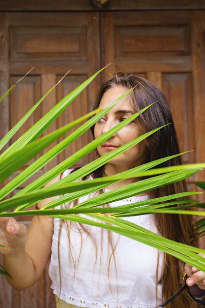 Una mujer mira desde detrás de una hoja de palma.