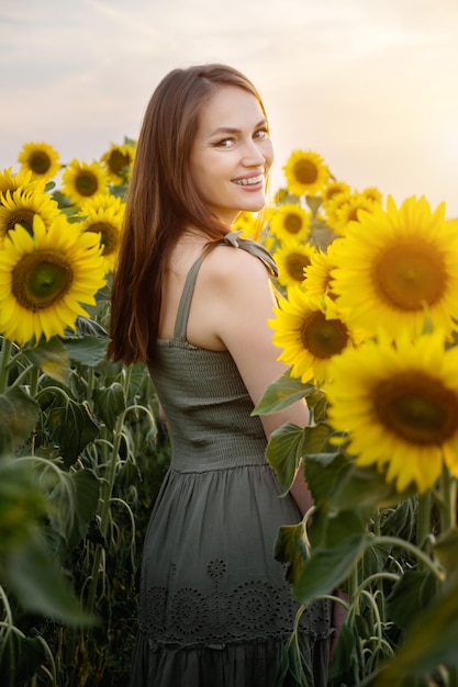 Mujer mira con expresión sonriente y feliz de pie contra el floreciente campo de girasol