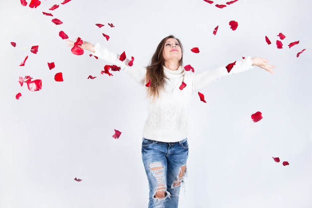 Foto la mujer mira felizmente la caída de pétalos de rosa, con los brazos extendidos a los lados