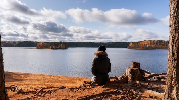 La mujer mira el lago con el bosque del otoño alrededor.